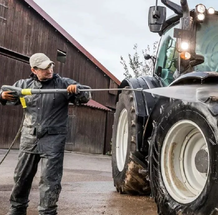 Mann mit K&auml;rcher Hochdruckreiniger reinigt Traktor